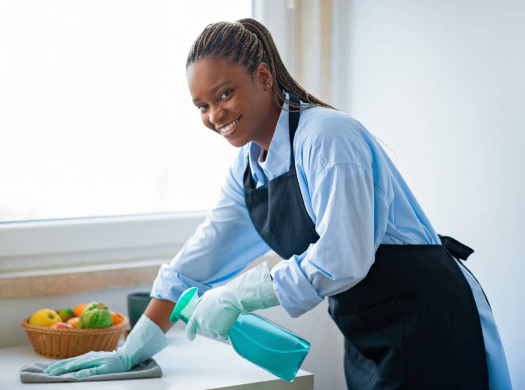 positive african american maid cleaning kitchen and smiling